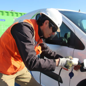 Hombre trabajador utilizando eco-cargador en camioneta eléctrica blanca