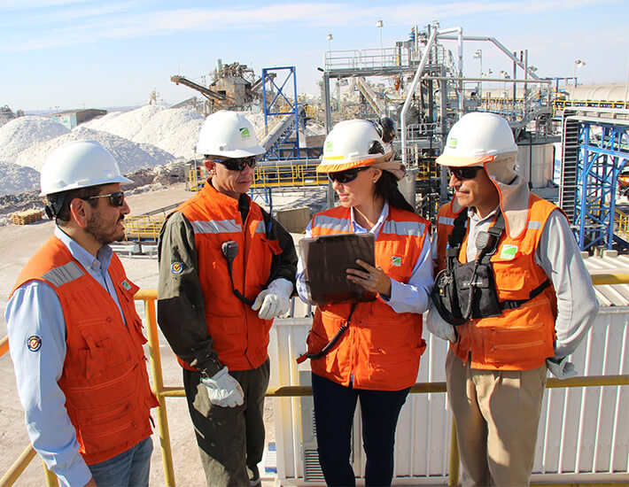 Imagen de cuatro trabajadores de SQM con una fábrica de litio en el fondo